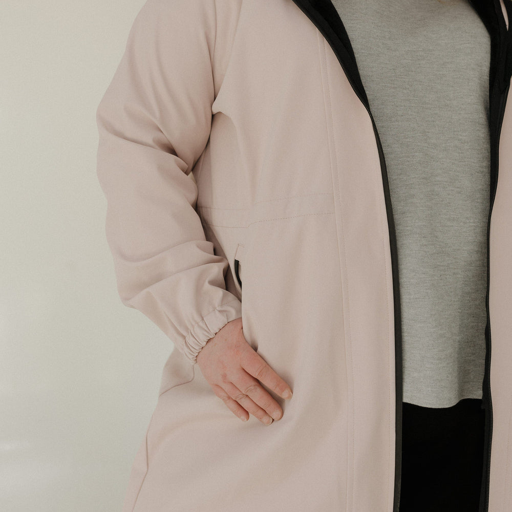 Person wearing a light pink coat over a gray shirt on a plain background