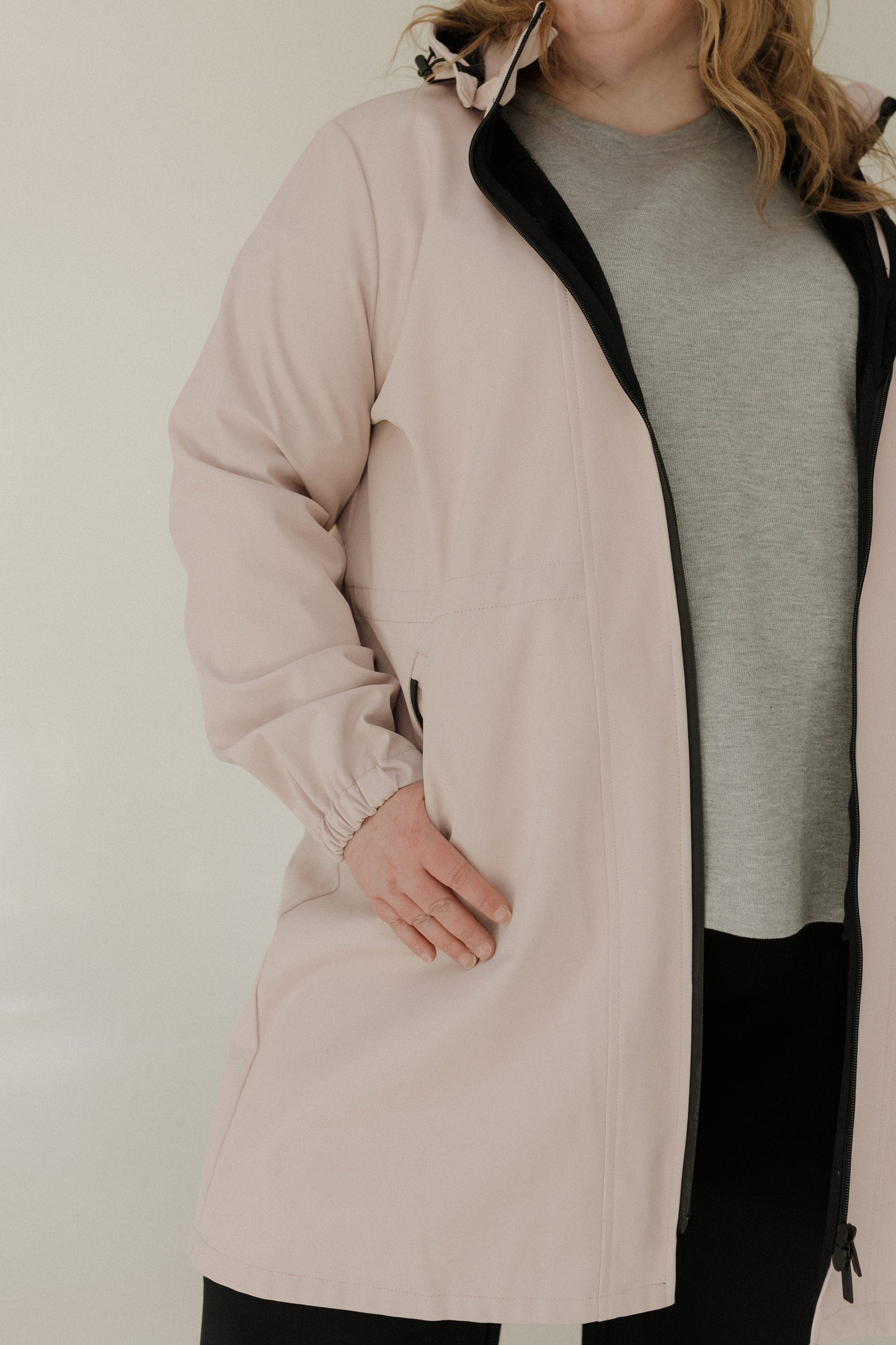 Person wearing a light pink coat over a gray shirt on a plain background