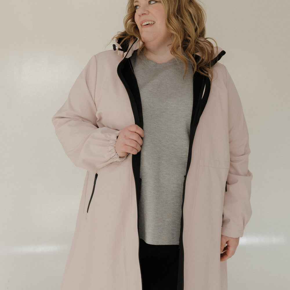 Person wearing a light pink coat with a black interior lining on a plain background