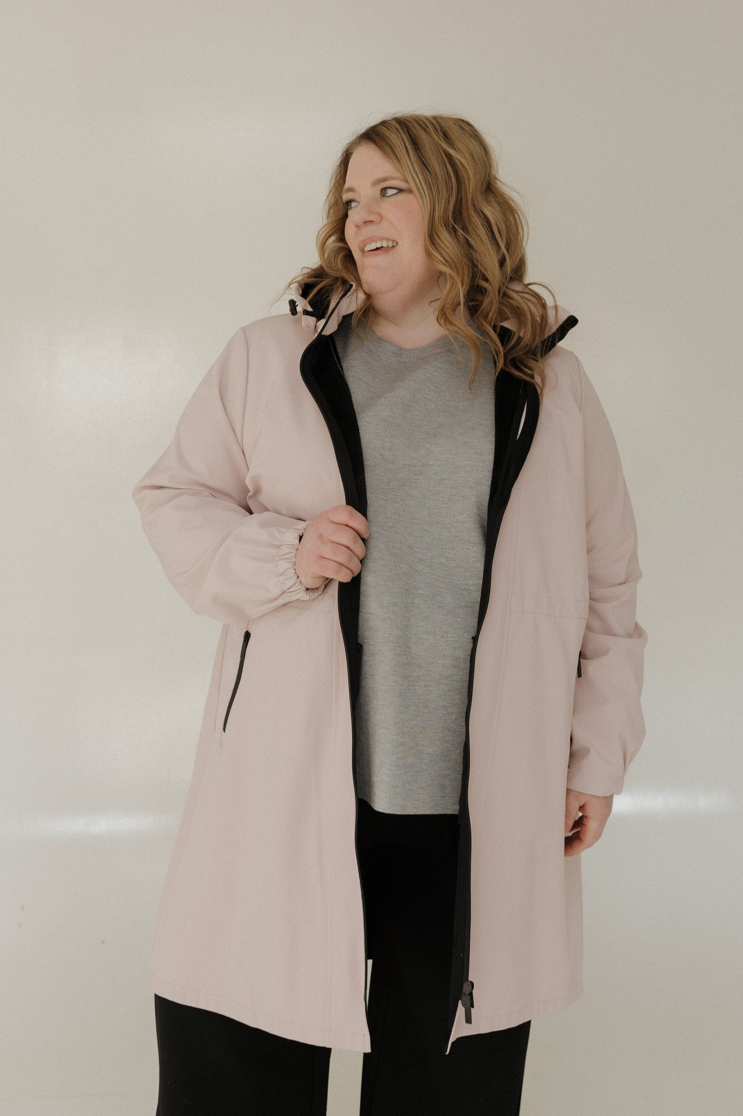 Person wearing a light pink coat with a black interior lining on a plain background