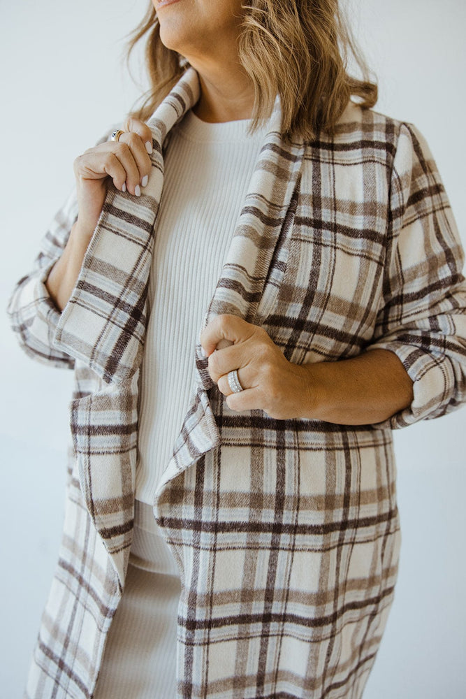 A person wearing the Andrea by Unit LIGHTWEIGHT PLAID MIDI BLAZER over a white outfit is shown adjusting the collar, displaying a ring on their finger.