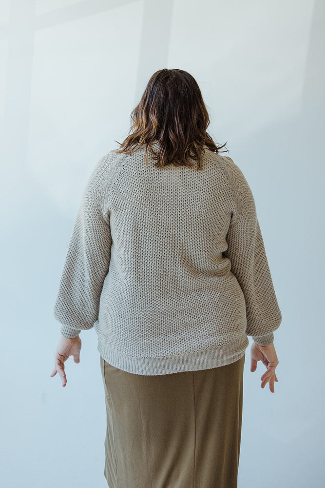 A person with shoulder-length hair is seen from behind, wearing Yesta's Lightweight Raglan Sleeve Turtleneck in Dried Sage with ribbed knit blouson cuffs and a brown skirt, against a light background.