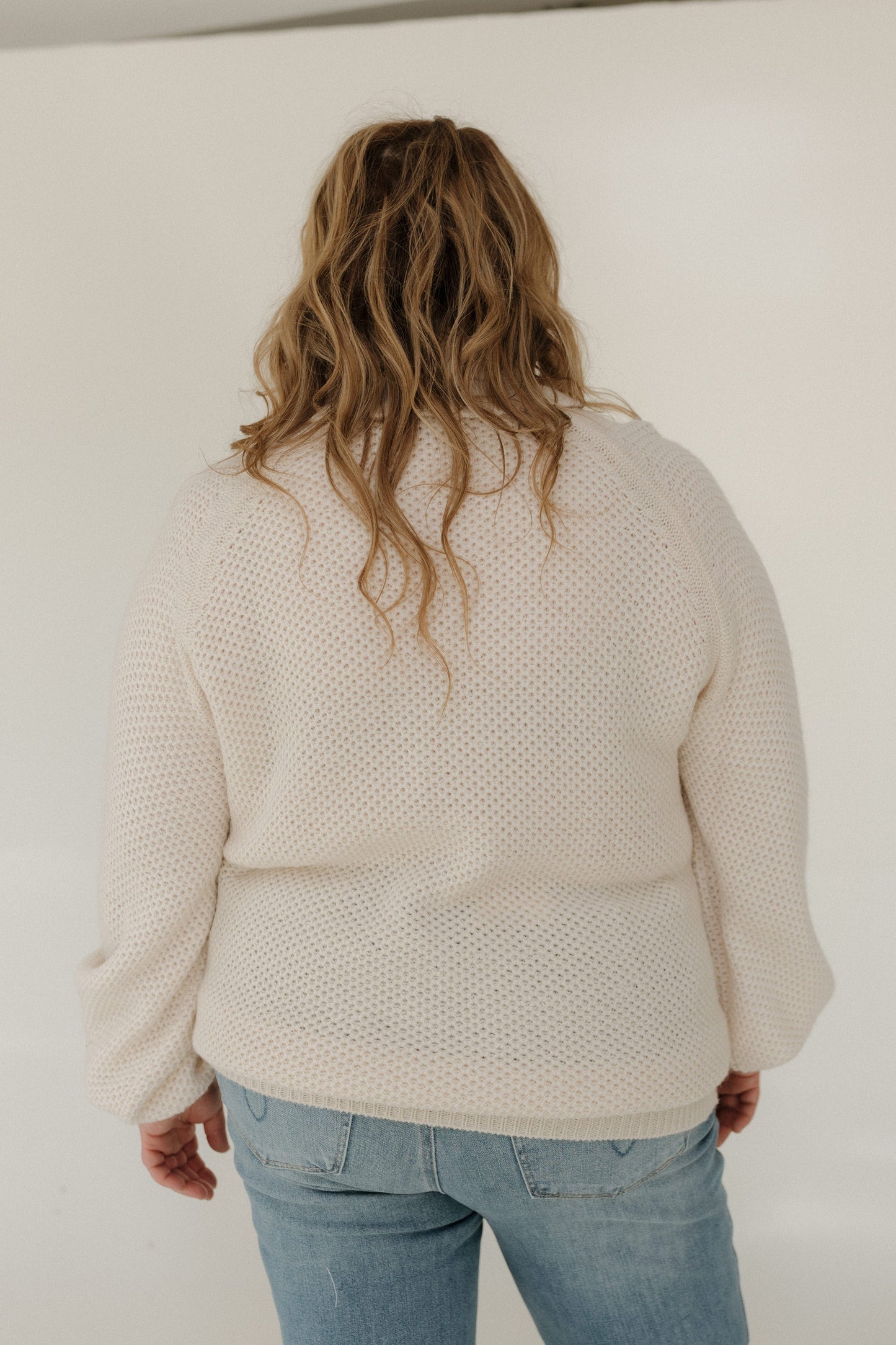 Person wearing a beige sweater and blue jeans against a white background