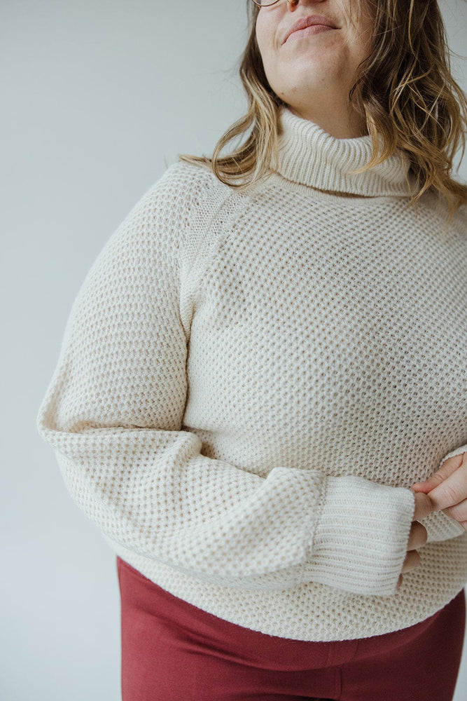 A person wearing the Yesta Lightweight Raglan Sleeve Turtleneck in Snowy White and red pants, standing against a light background.