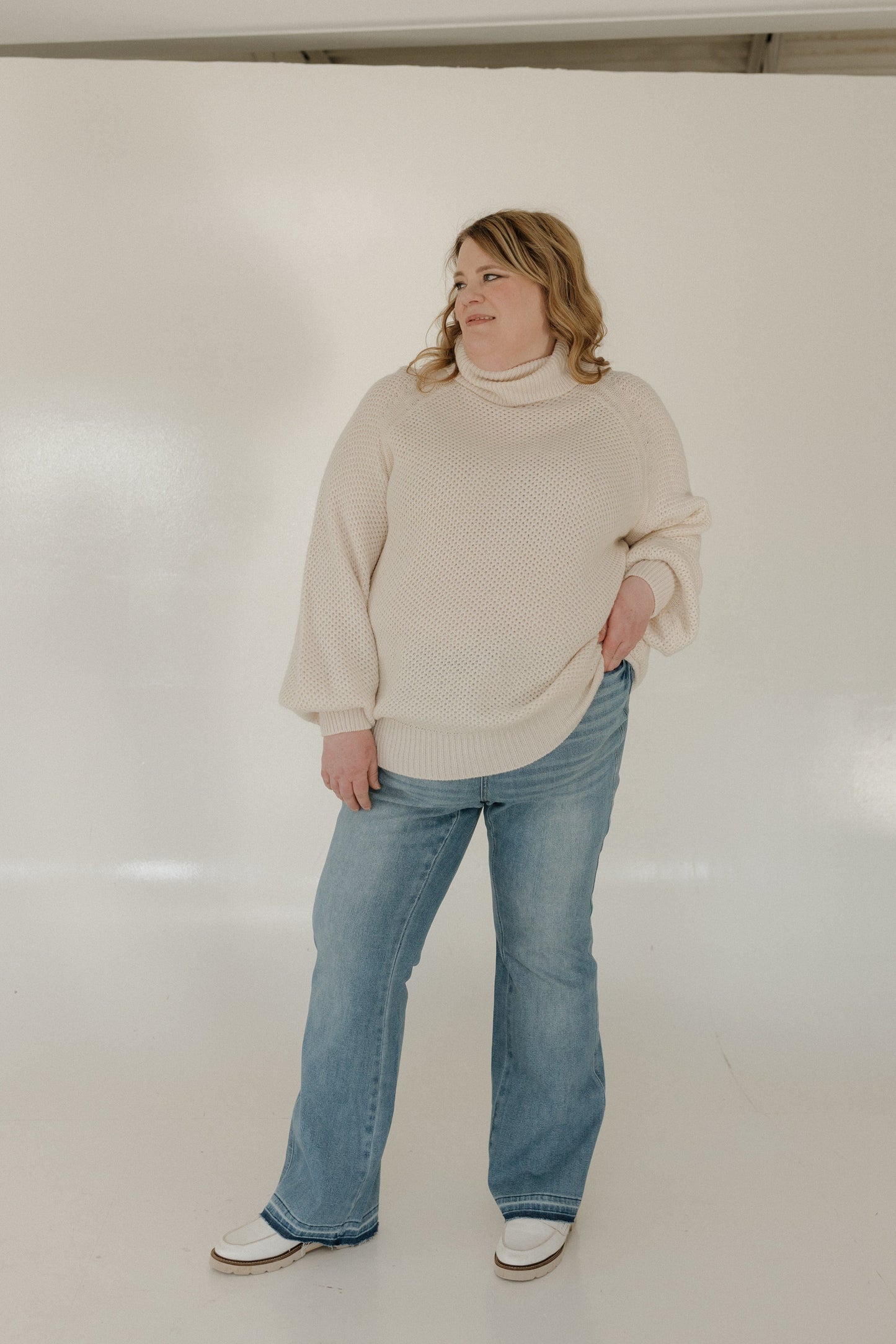 Person wearing a beige sweater and blue jeans against a white background
