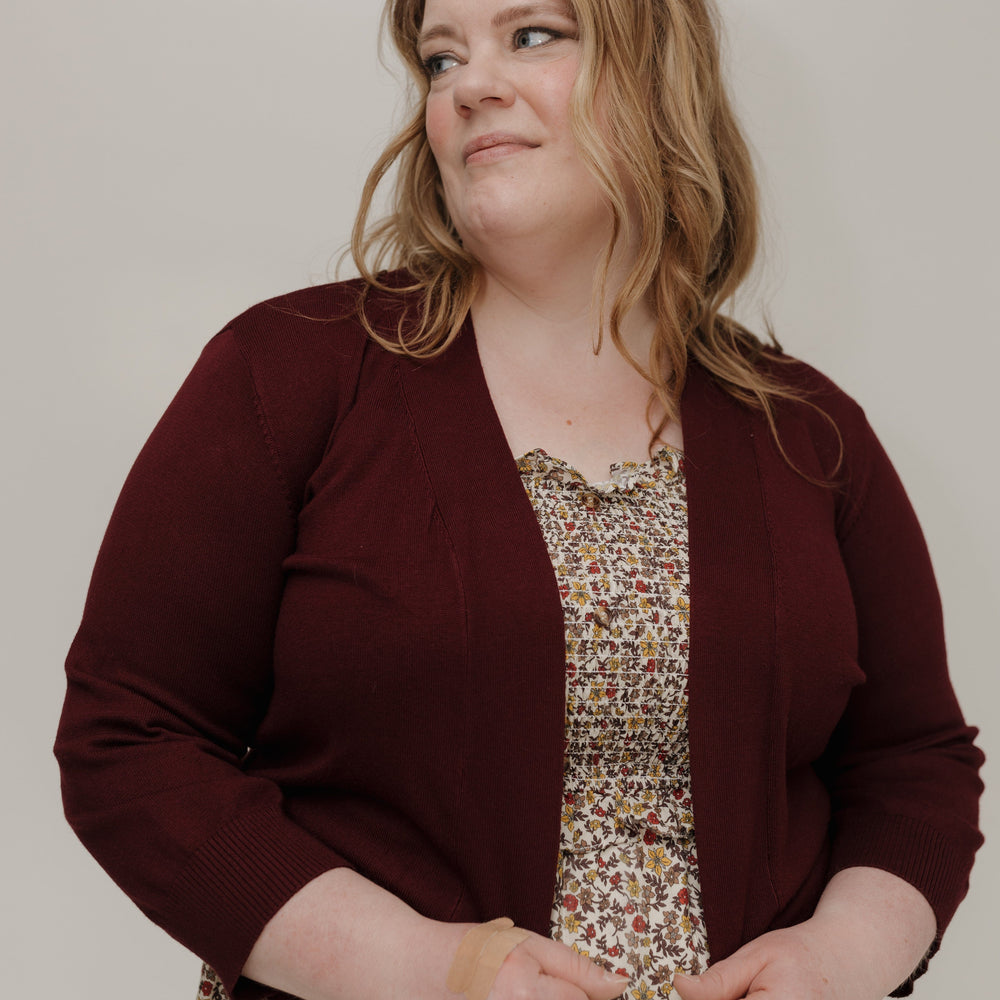 Woman wearing a maroon cardigan over a patterned dress against a plain background