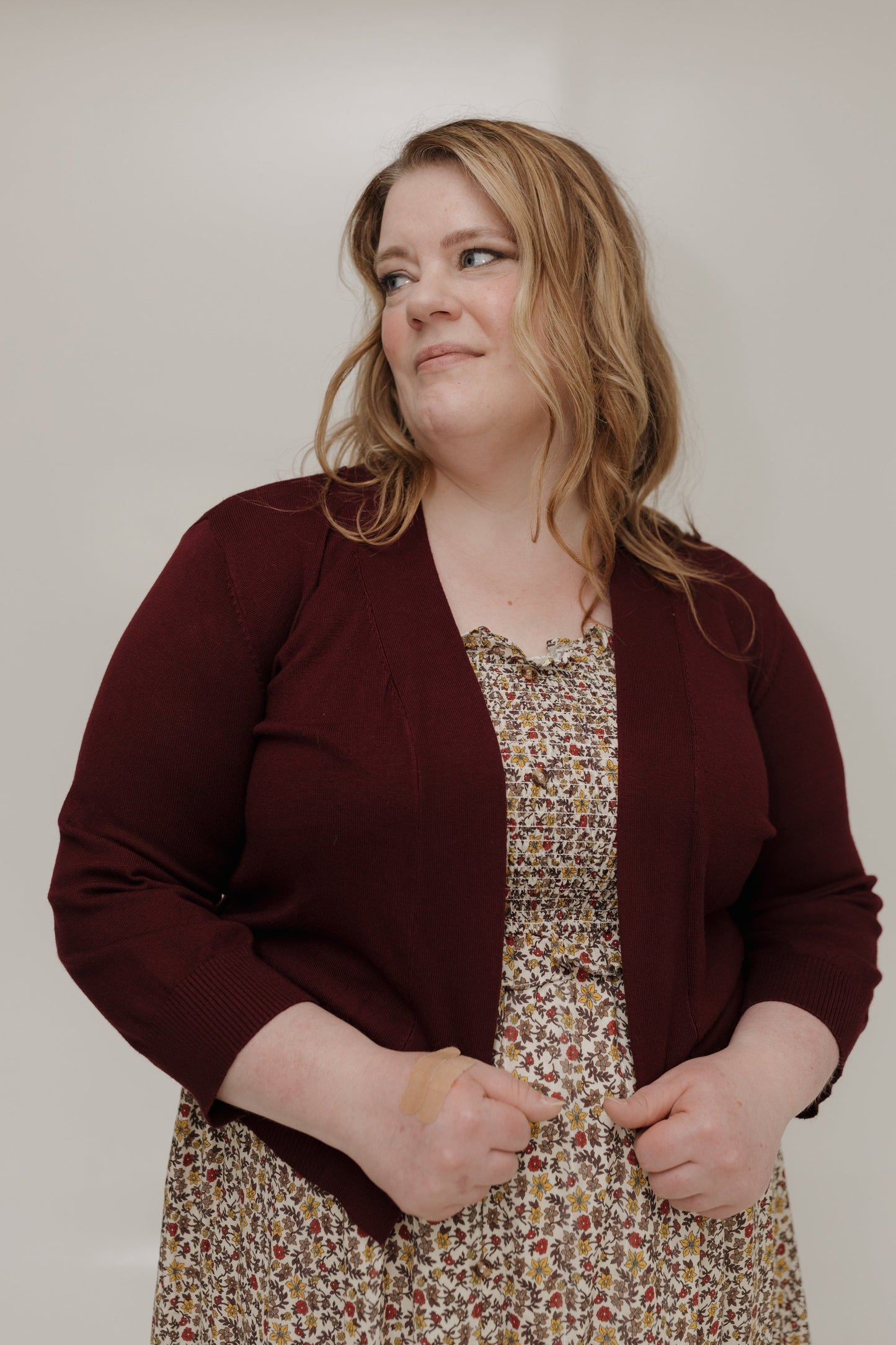 Woman wearing a maroon cardigan over a patterned dress against a plain background