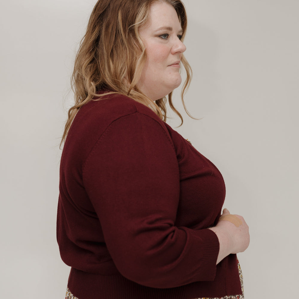Woman wearing a maroon sweater and floral skirt against a plain background