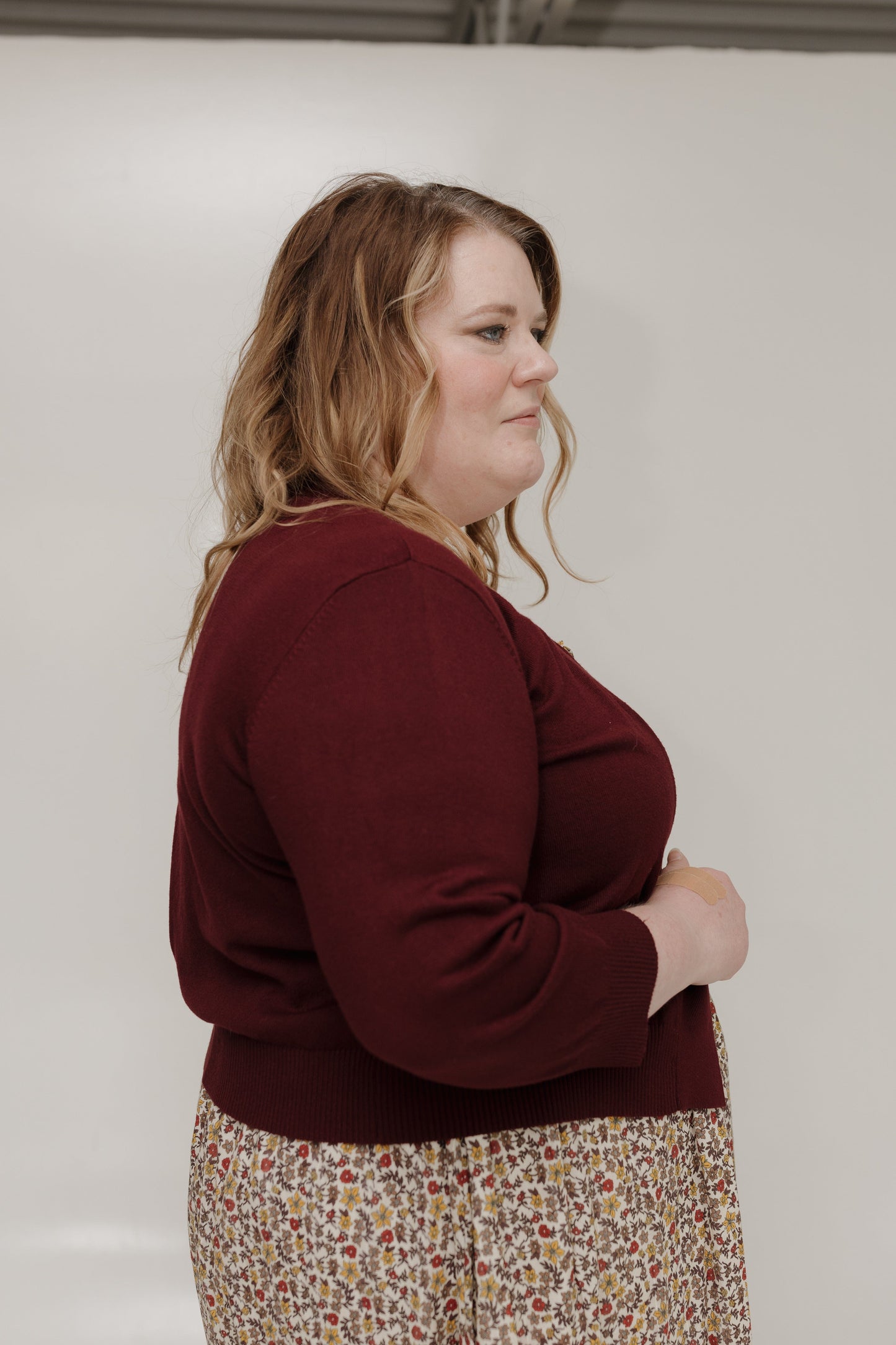 Woman wearing a maroon sweater and floral skirt against a plain background