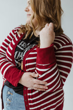 A person with long hair wearing the Zenana Lightweight Striped Snap Cardigan in cranberry and ivory and a denim skirt is standing with their back facing the camera.