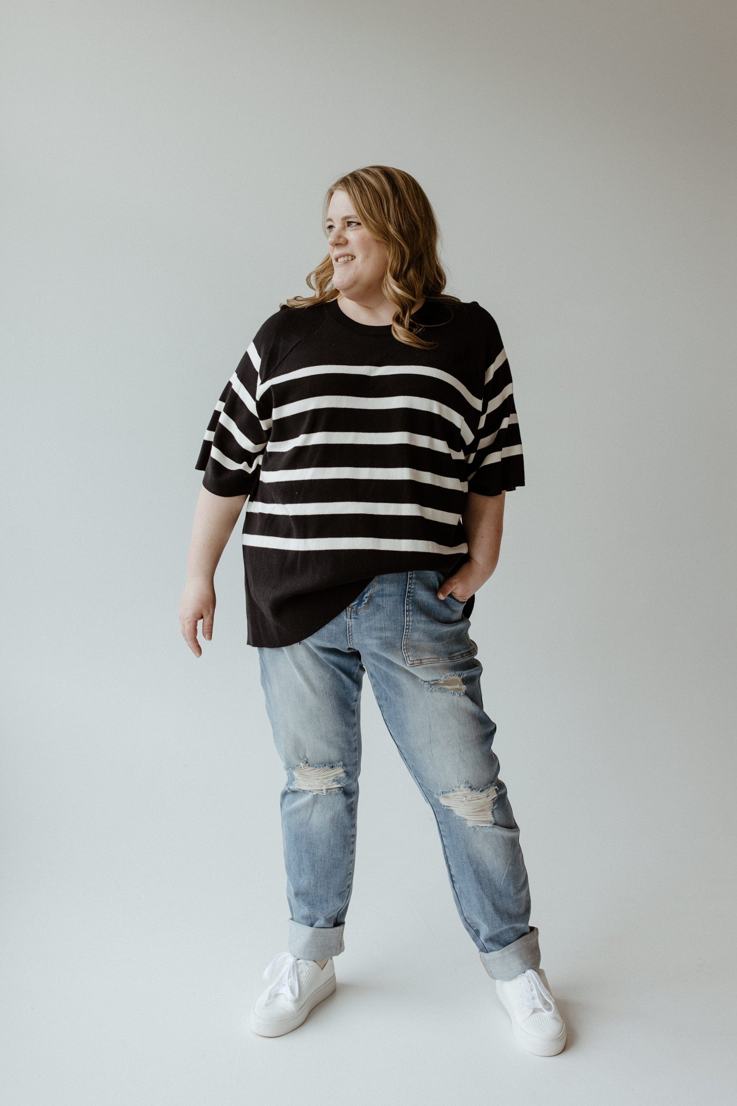A woman wearing the Yesta Lightweight Stripe Sweater in black and ecru, featuring an elegant round neckline, exudes effortless sophistication.