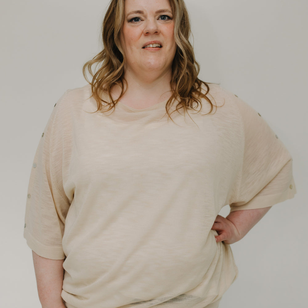 Person wearing a beige sweater and jeans against a plain background