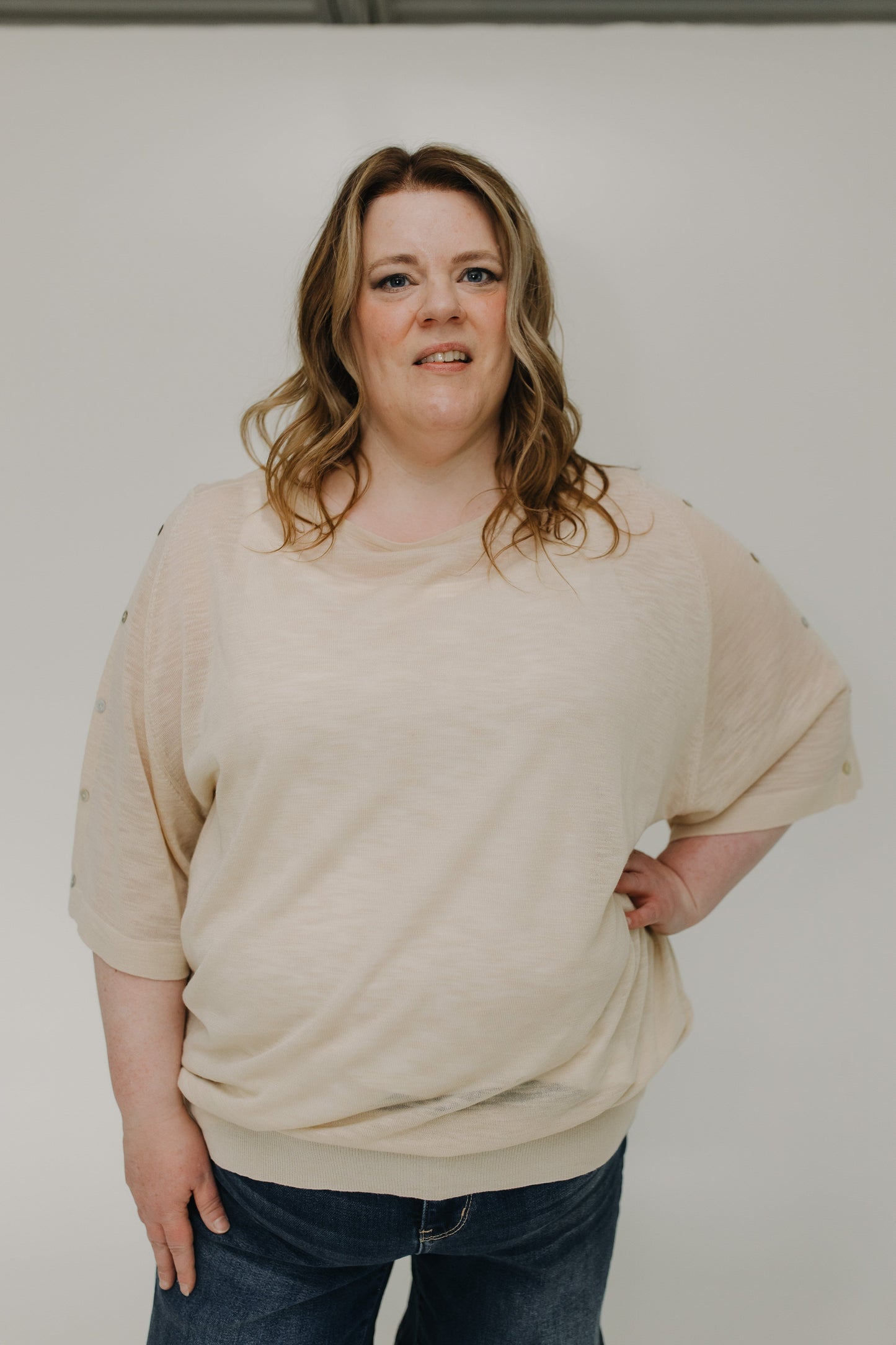 Person wearing a beige sweater and jeans against a plain background