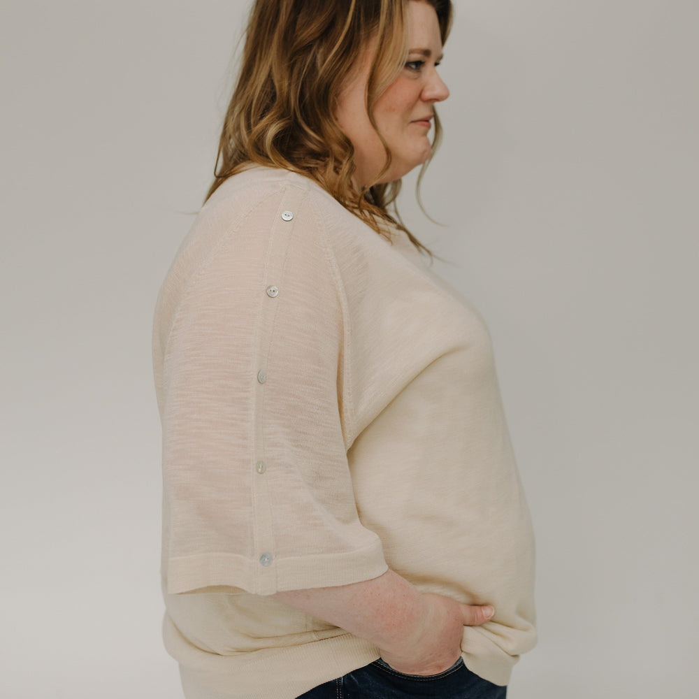 Woman wearing a beige sweater and blue jeans against a plain background