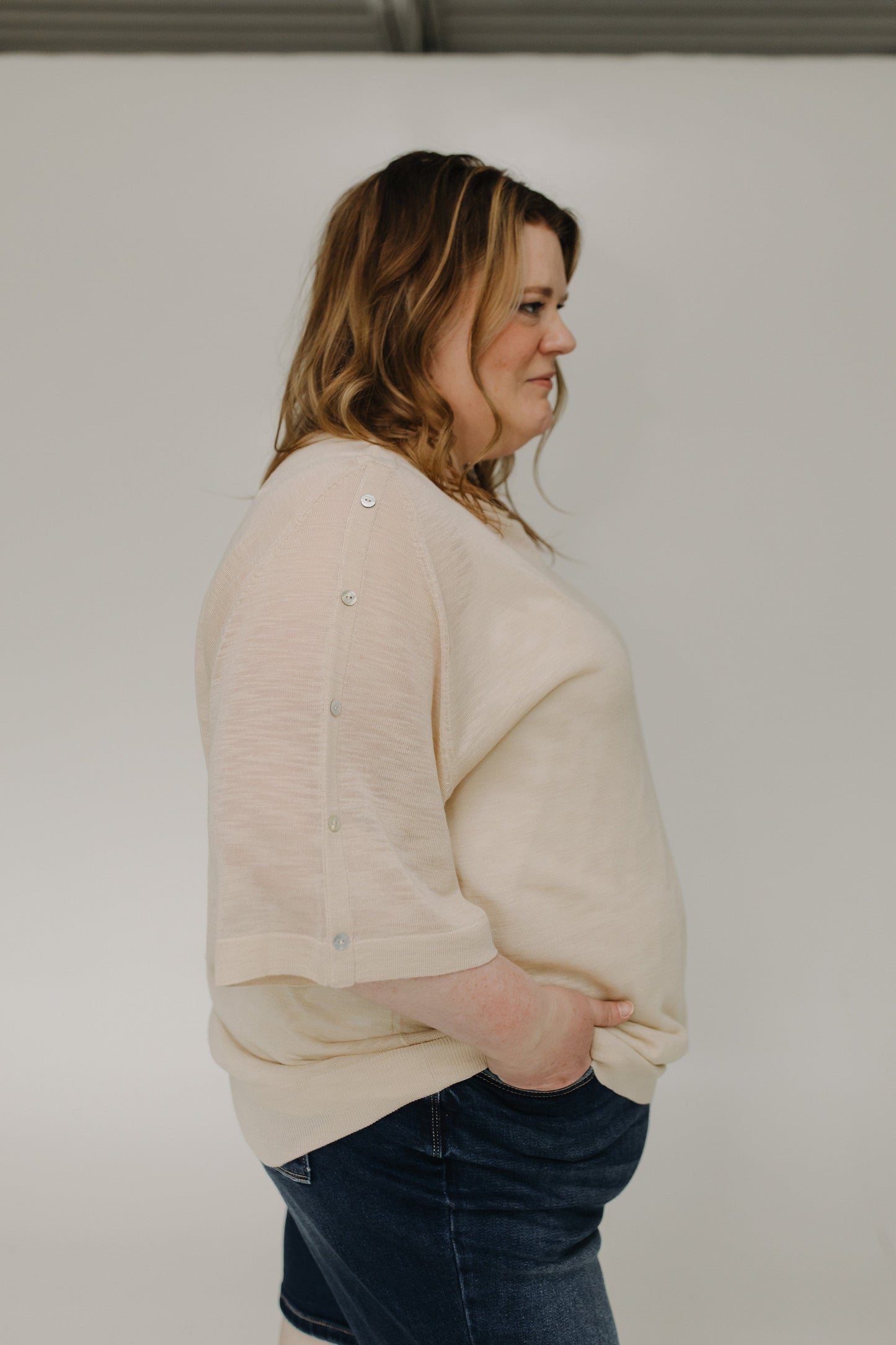 Woman wearing a beige sweater and blue jeans against a plain background