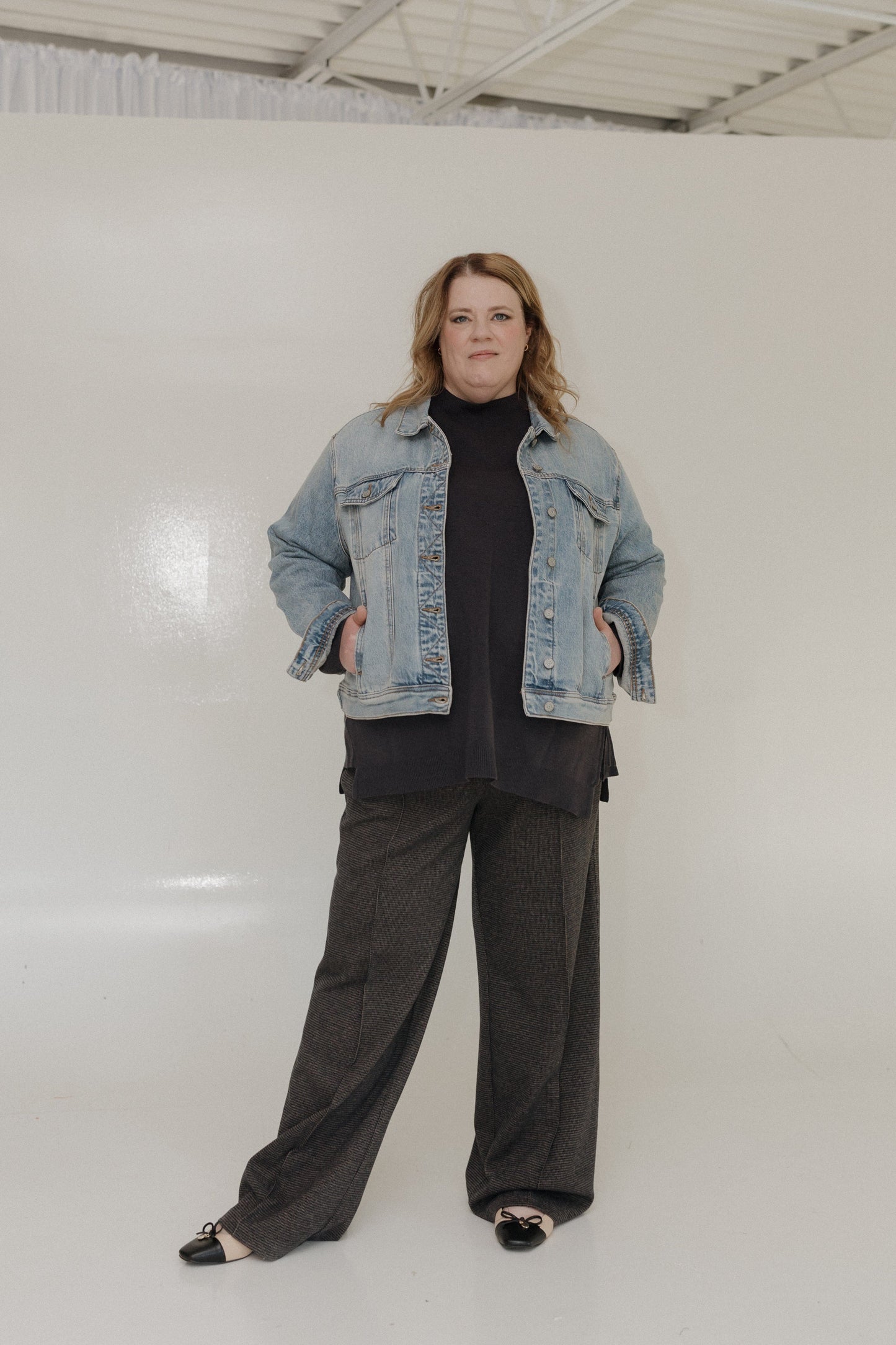 Person wearing a denim jacket over a black top and gray pants on a white background