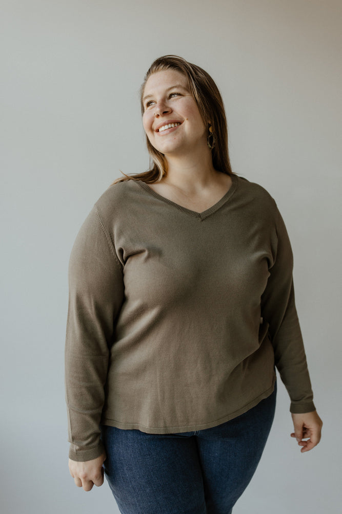 A person clad in the Lightweight V-Neck Sweater in Soft Army by Yesta and a pair of jeans, smiling while looking to the side against a plain background.