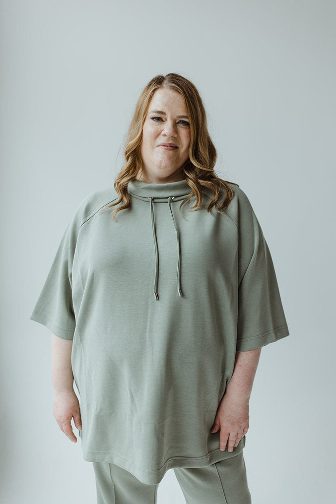 A person with long, wavy hair stands with their back to the camera, wearing a LIGHT AS AIR COWL NECK TEE IN ECHEVERRIA by Yesta, which drapes beautifully for a comfortable oversized fit and pairs perfectly with matching pants.