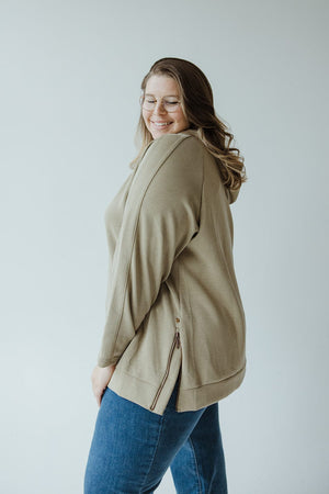 A person with long hair and glasses is wearing a LIGHT AS AIR DOUBLE-STRING HOODIE IN OM GREEN from Yesta and blue jeans. They are smiling and standing against a plain background.