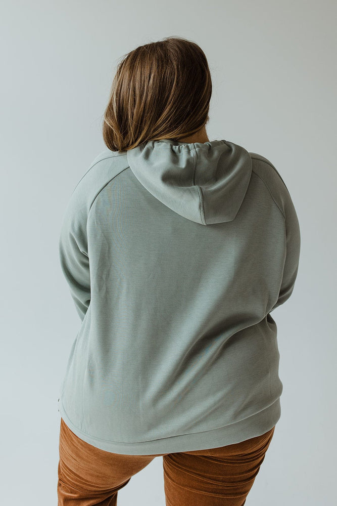 Person wearing the LIGHT AS AIR DOUBLE-STRING HOODIE IN QUIETUDE by Yesta and brown pants, standing with their back to the camera against a neutral background, exemplifying contemporary leisurewear.