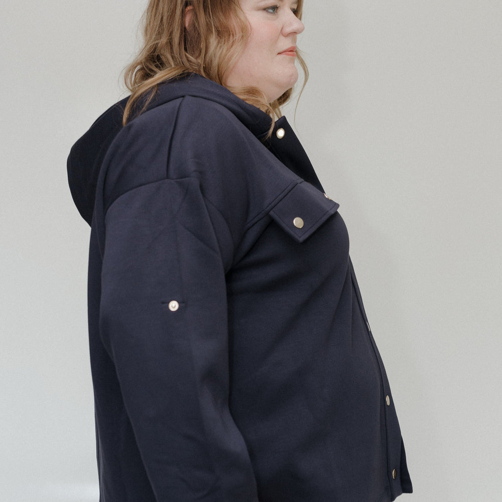 Person wearing a navy blue jacket with a hood on a plain background