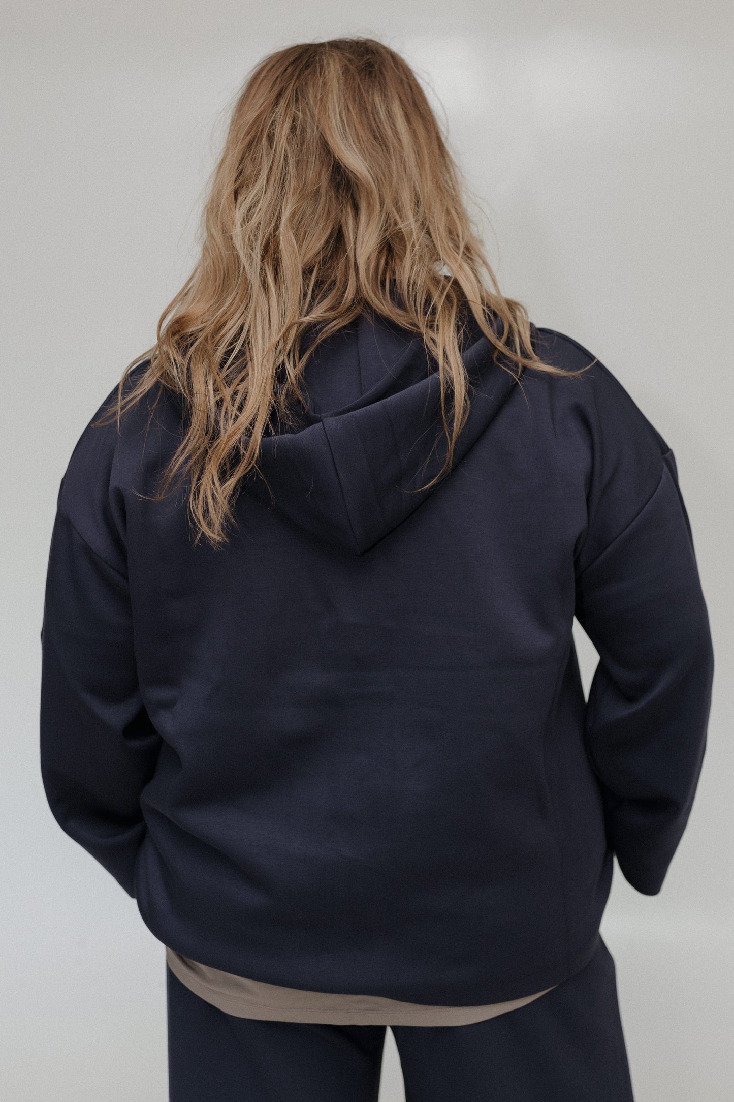 Person wearing a dark blue hoodie from behind on a plain background