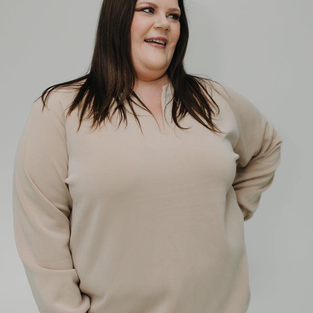 Woman wearing a beige sweater and blue jeans against a plain background