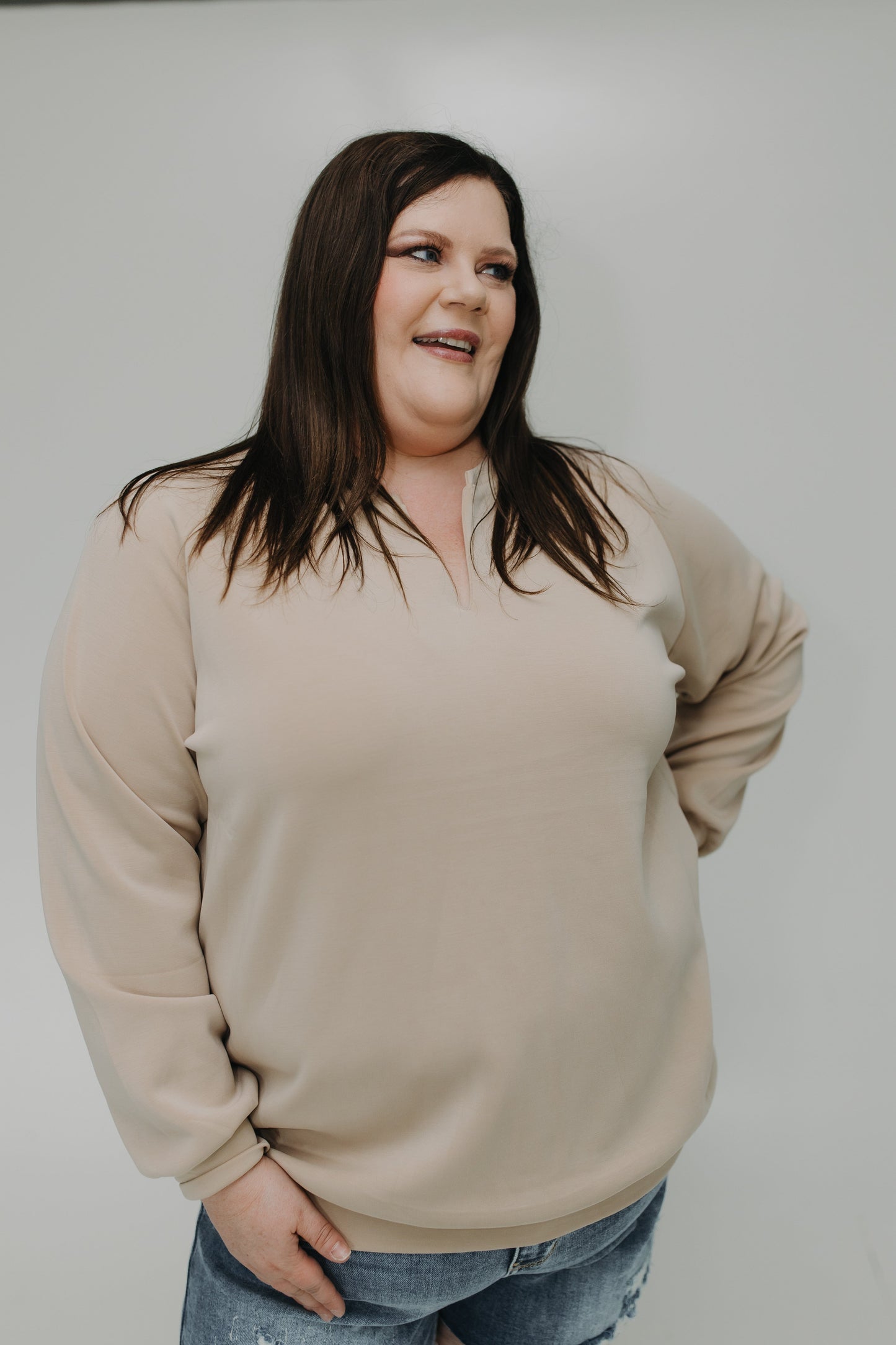 Woman wearing a beige sweater and blue jeans against a plain background