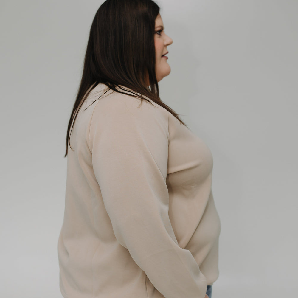 Woman wearing a beige sweater and blue jeans against a plain background