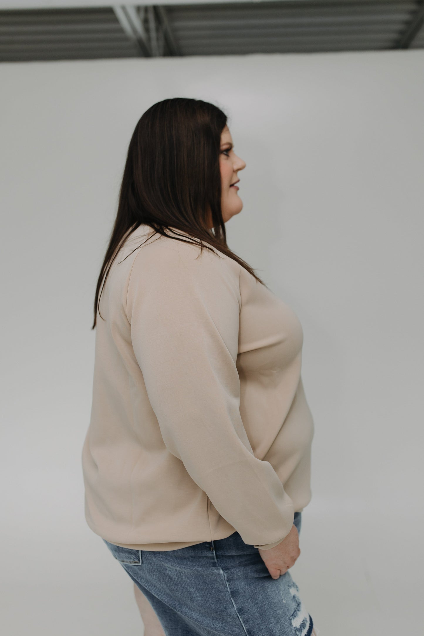 Woman wearing a beige sweater and blue jeans against a plain background