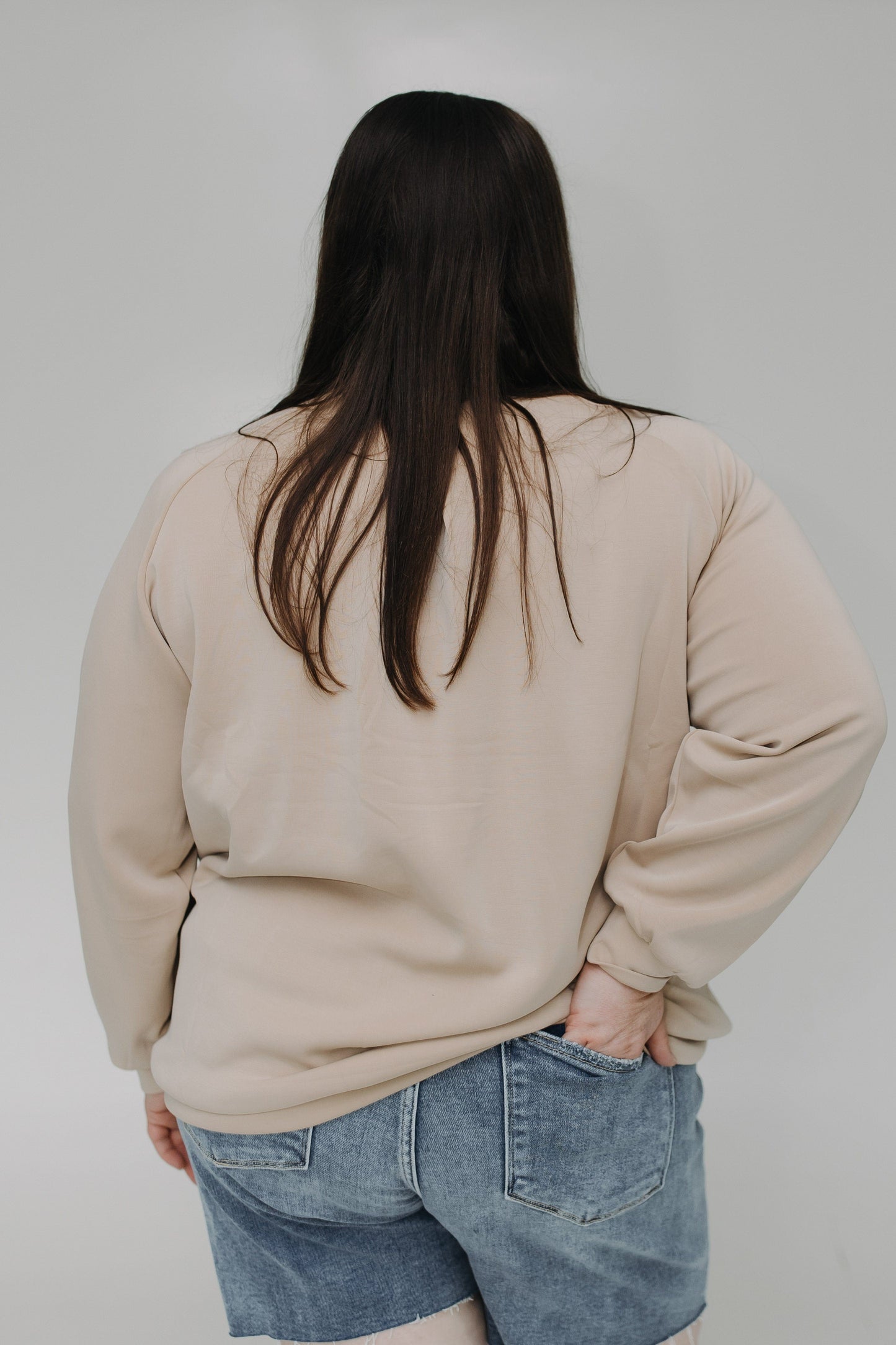 Person wearing a beige sweatshirt and blue jeans from behind on a plain background