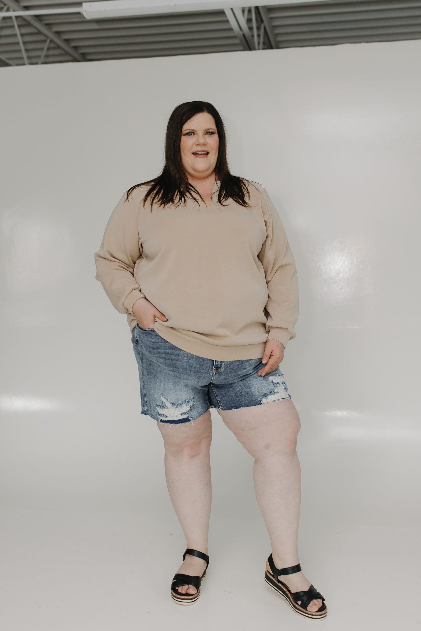 Person wearing a beige sweater and denim shorts against a white background