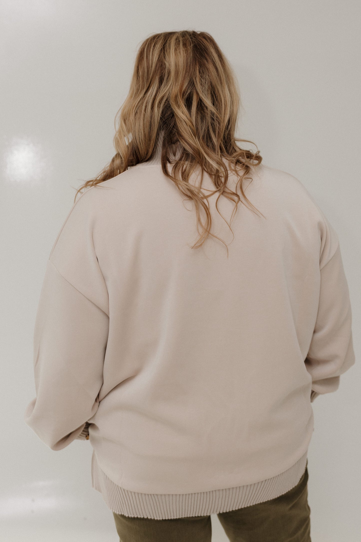 Person wearing a beige sweater from behind on a plain background