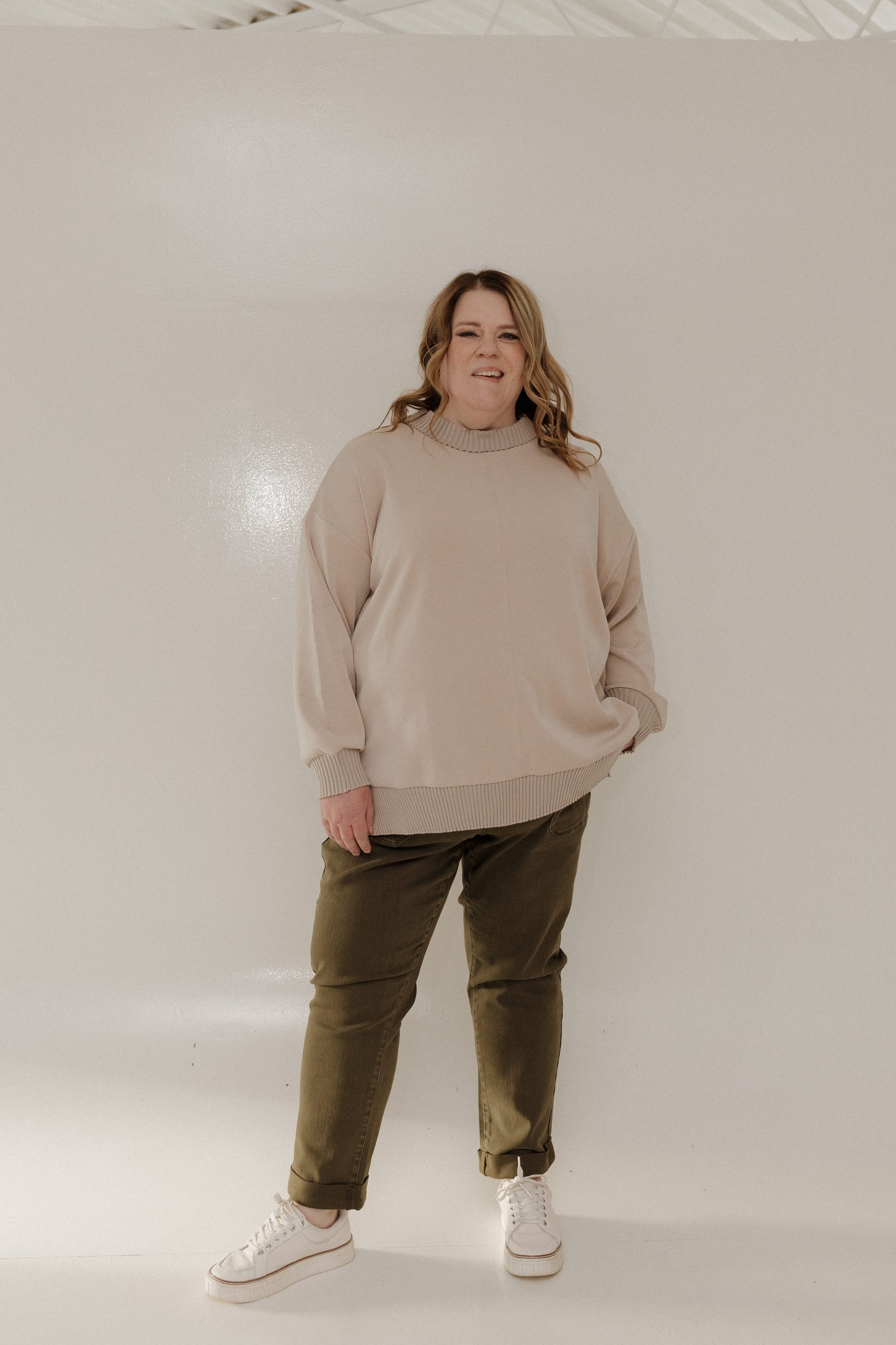 Person wearing a beige sweater and green pants on a plain background
