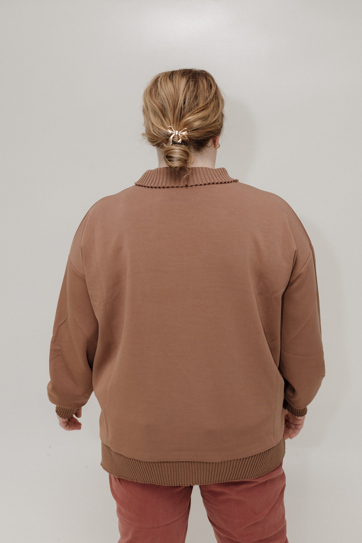 Person wearing a brown sweater and pants against a plain background