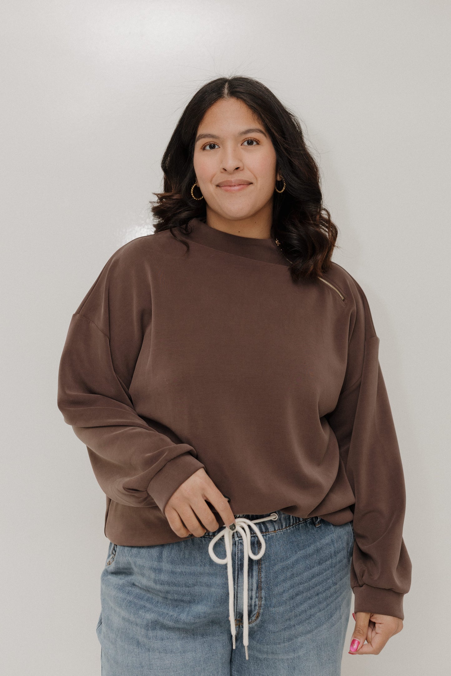 Person wearing a brown sweatshirt and blue jeans against a plain background