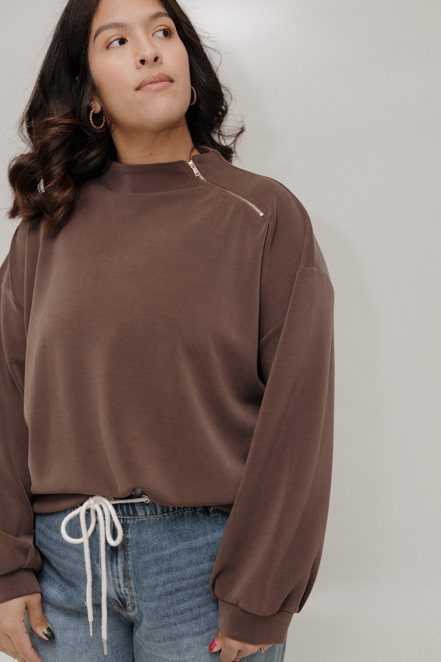 Woman wearing a brown long-sleeve top with a zipper on a plain background