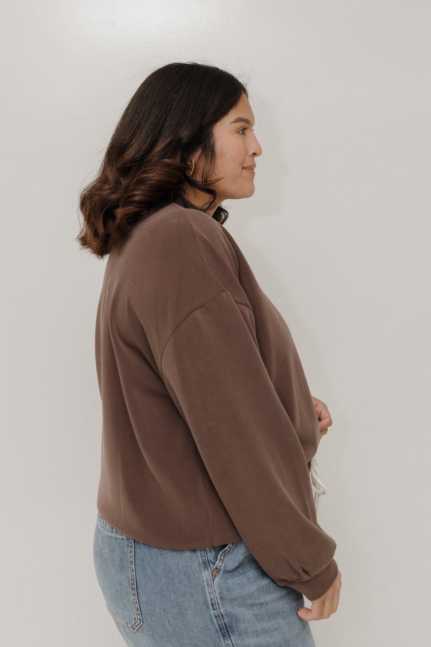 Person wearing a brown sweatshirt and blue jeans against a white background