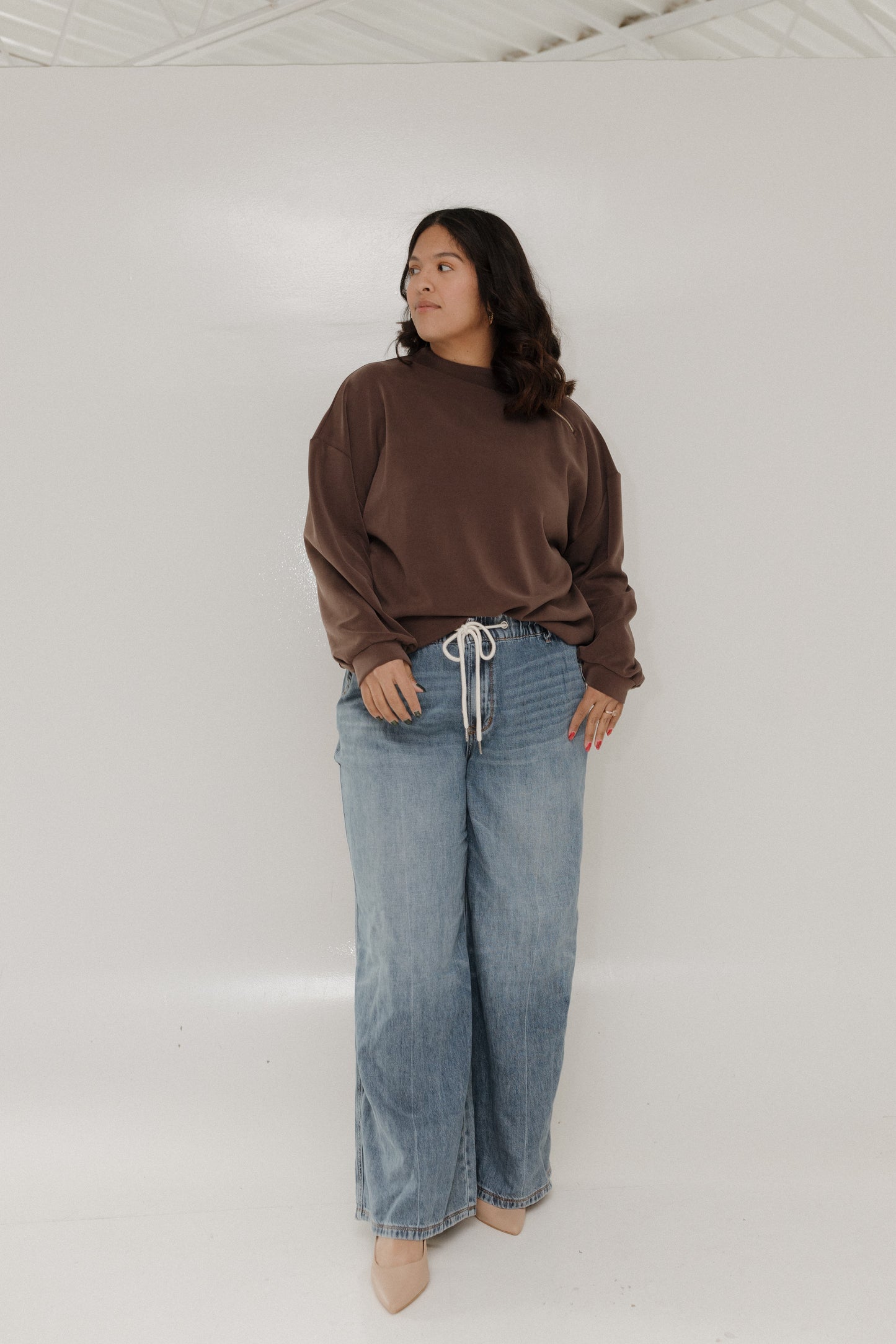 Person wearing a brown sweater and blue jeans against a white background
