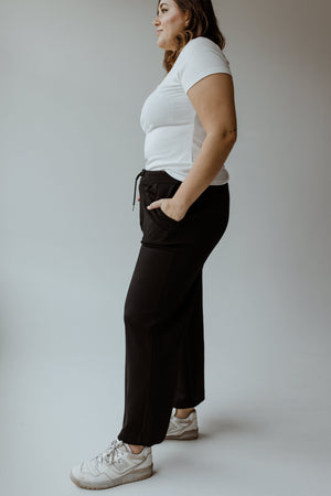 A person in a white t-shirt, Yesta's LIGHT AS AIR PLEATED WIDE LEG PANTS with an elastic waistband, and white sneakers stands sideways with hands in pockets against a plain background.