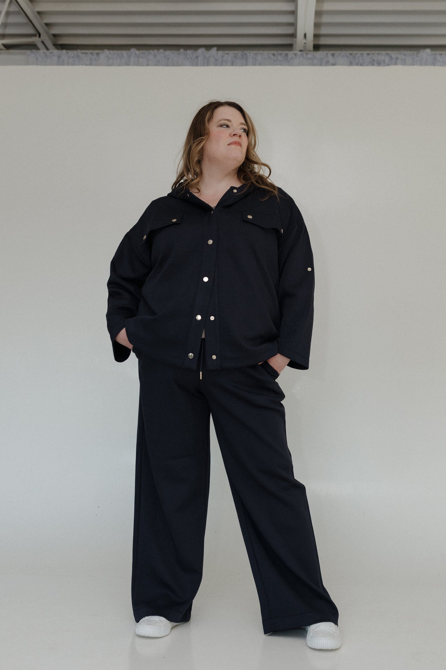Person wearing a black outfit with white buttons against a plain background