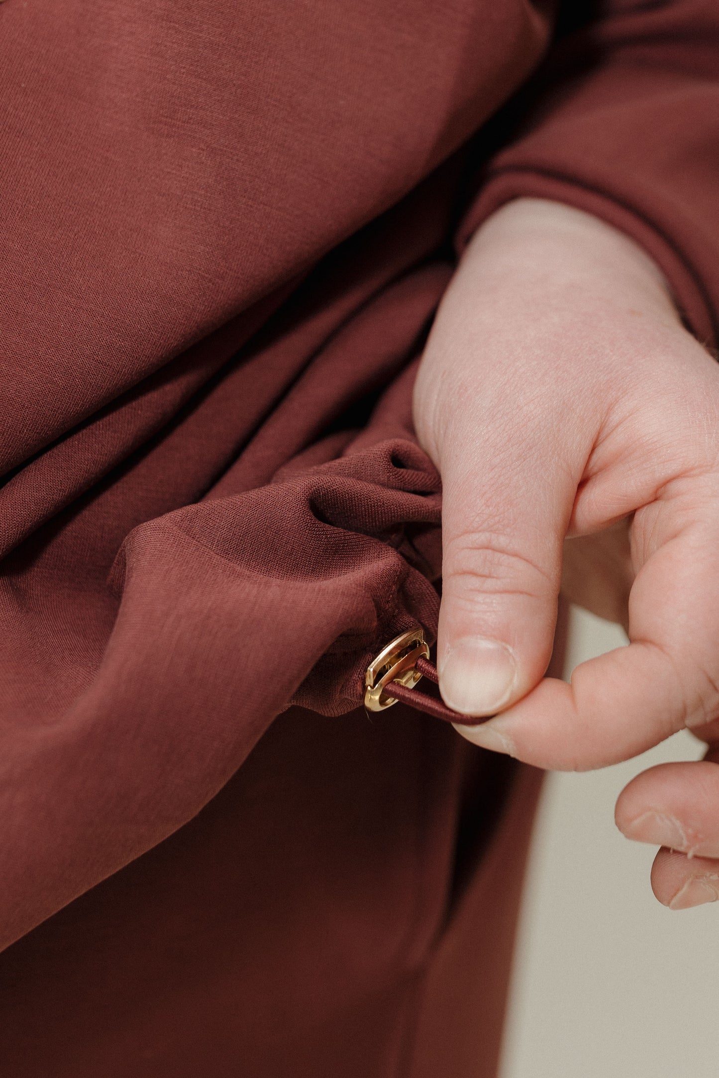 Close-up of a hand adjusting a gold zipper on a brown garment.