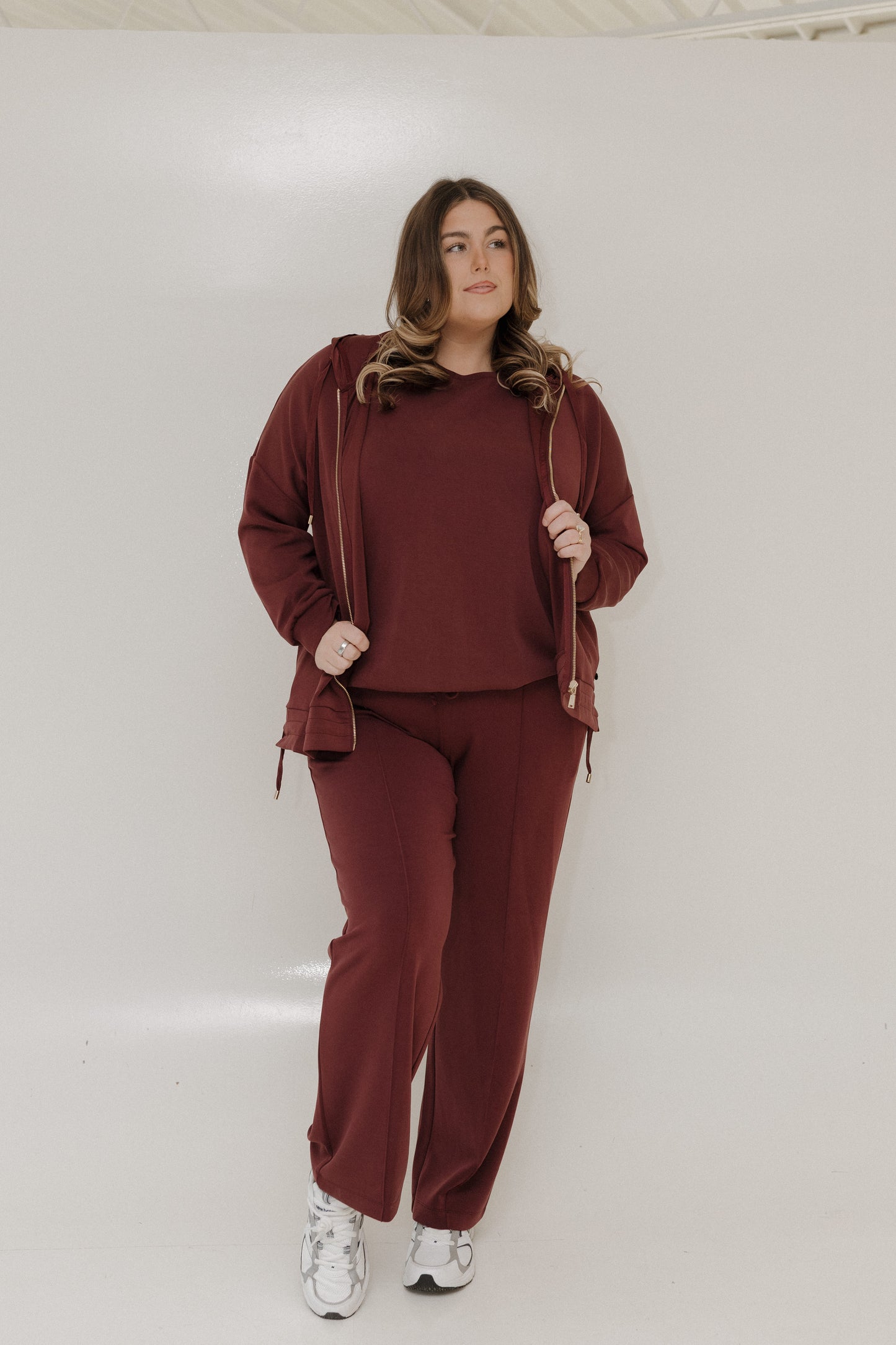 Woman wearing a maroon tracksuit against a white background