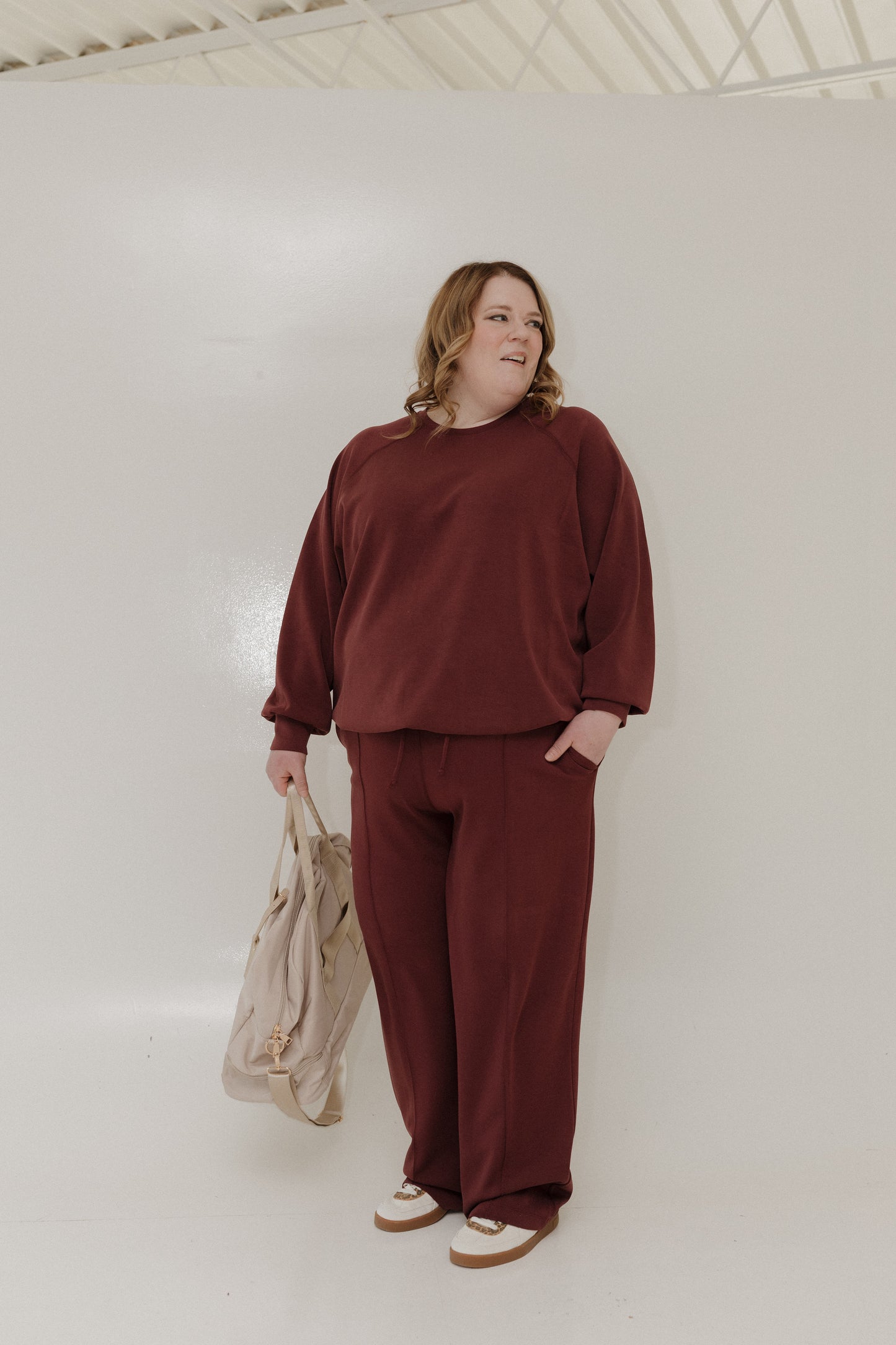 Person wearing a maroon outfit holding a beige bag against a white background