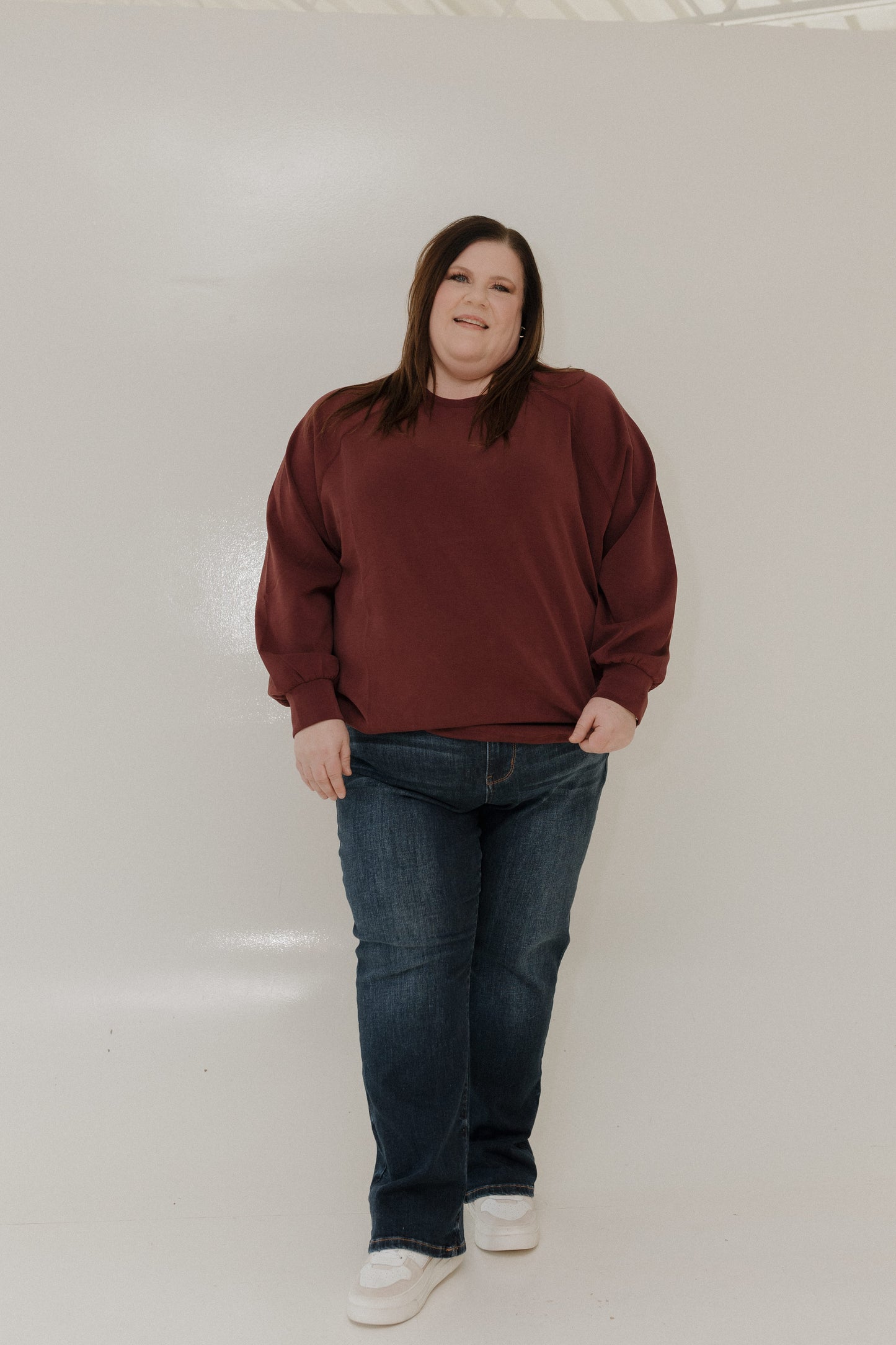 Person wearing a maroon sweatshirt and blue jeans standing against a plain background