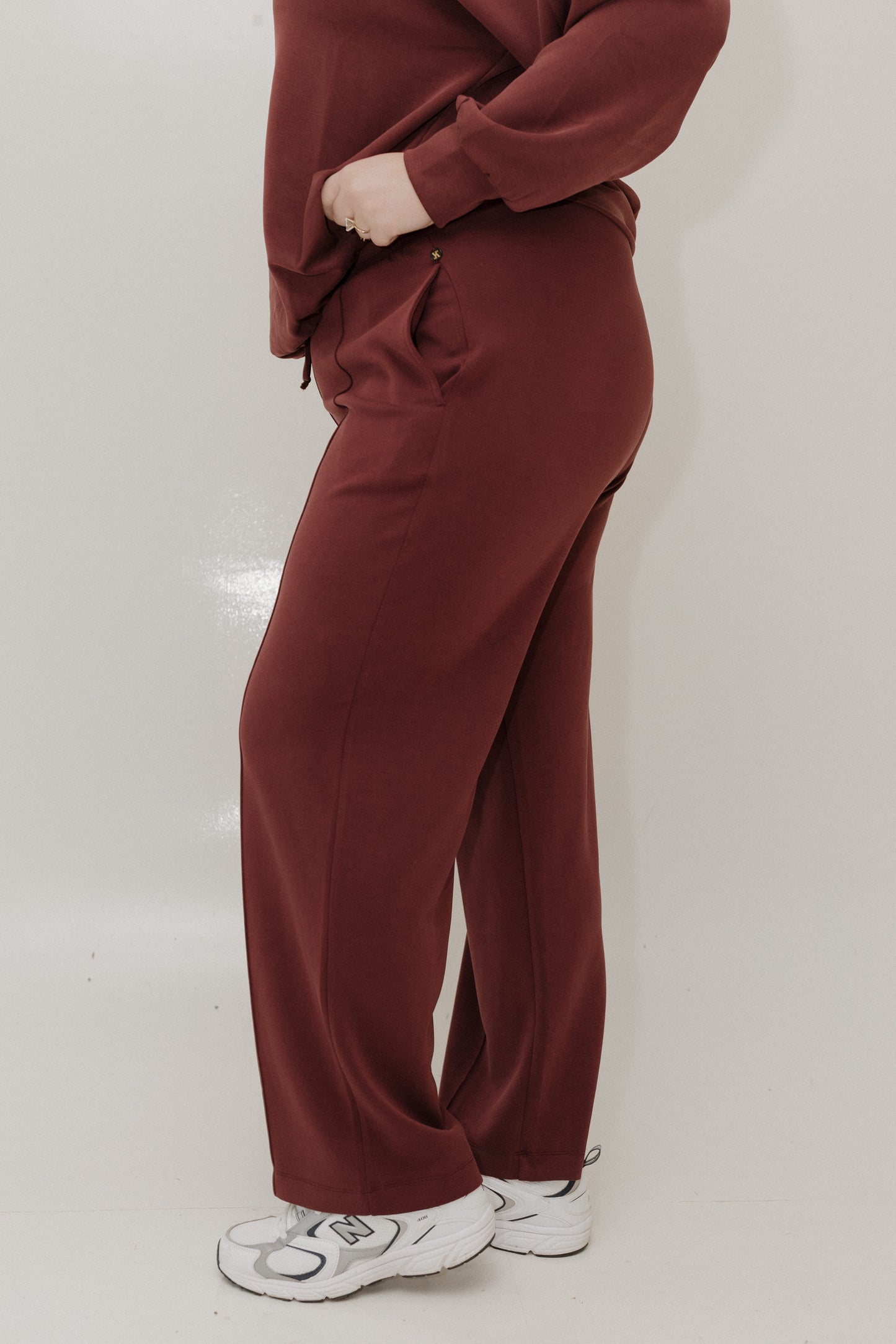 Person wearing a maroon tracksuit with white sneakers on a light background