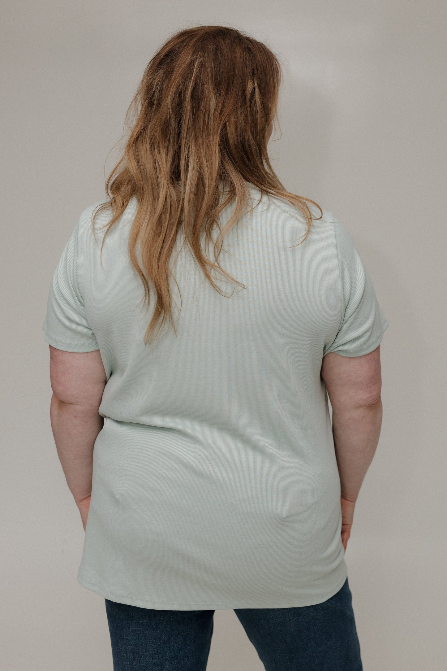 Person wearing a light green t-shirt and blue jeans against a plain background