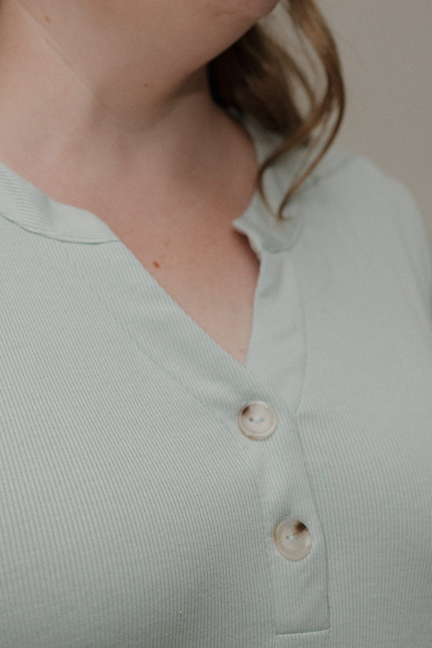 Light green shirt with buttons worn by a person, blurred background