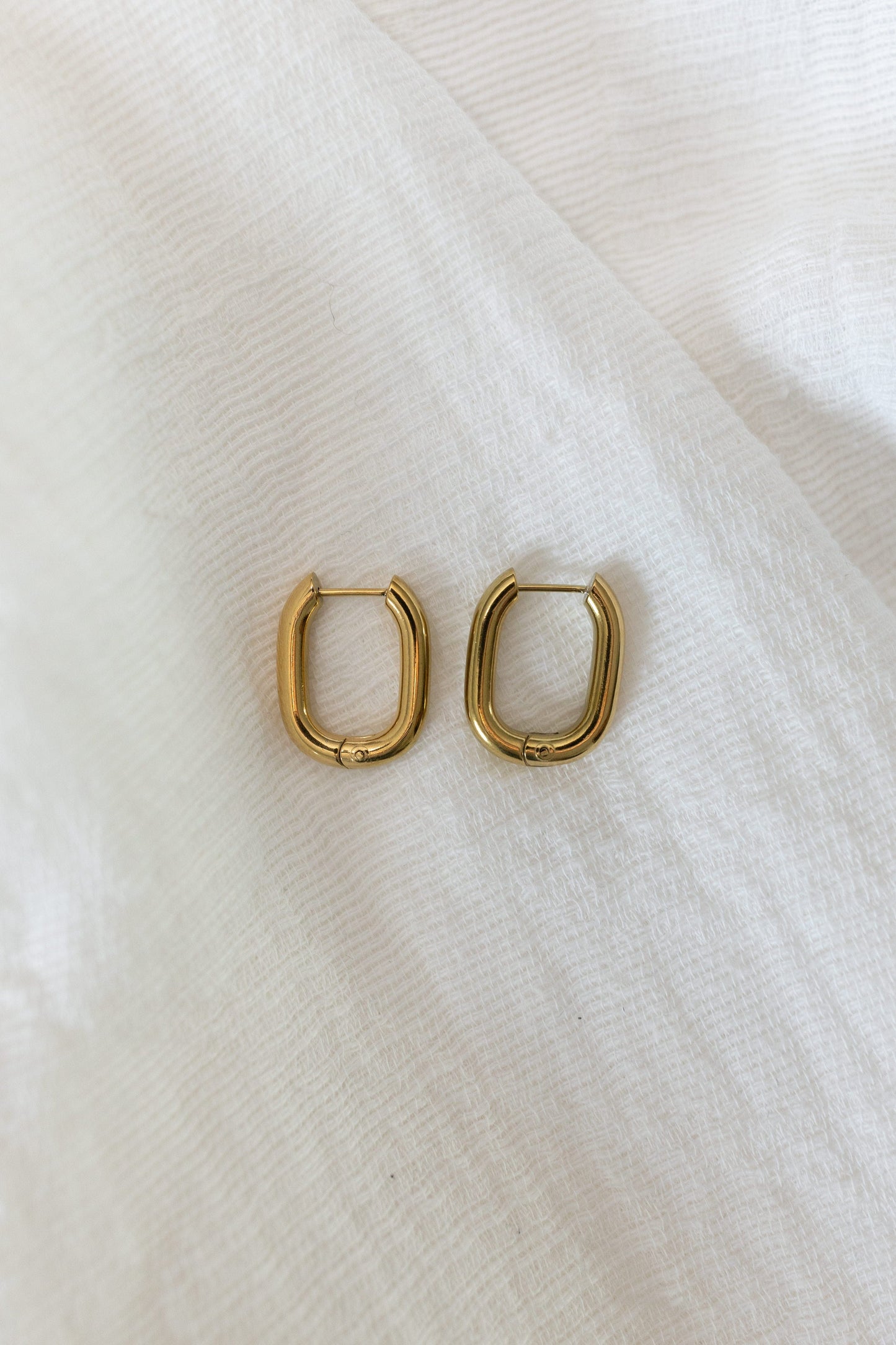 Gold hoop earrings on a white fabric background