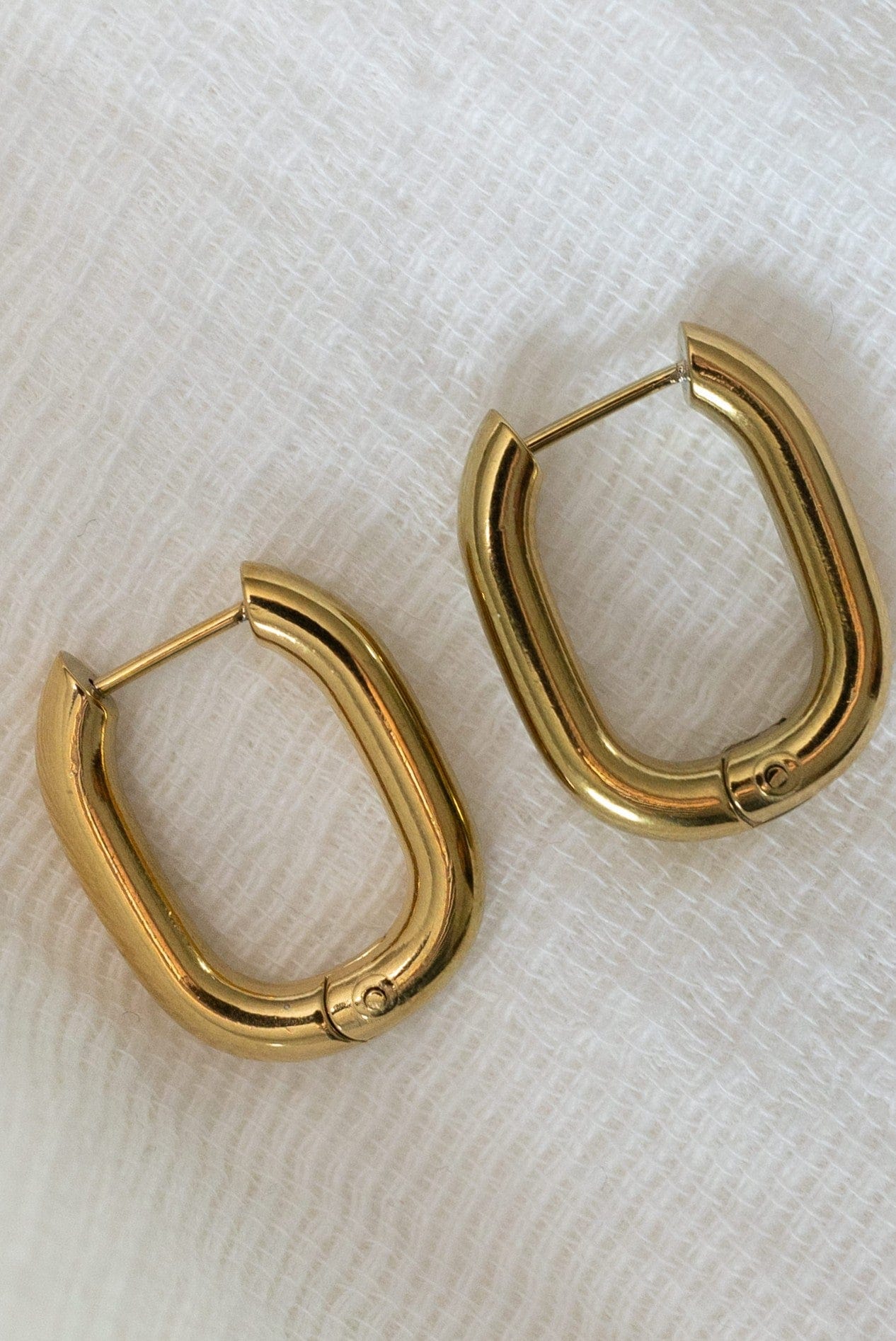 Gold hoop earrings on a white textured fabric background